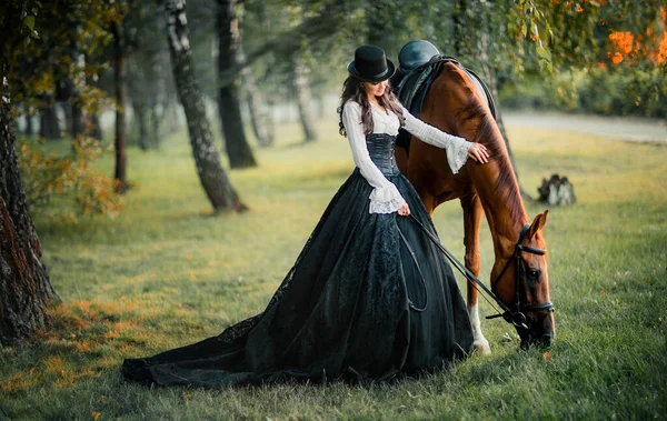 馬を歩いて壮大なファッションゴシック少女の肖像 ファンタジーアートワークとフェアリー 黒白のドレスと帽子のポーズで素晴らしいブルネットモデル — ストック写真