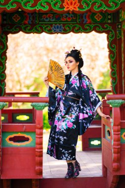 Pagoda yakınlarındaki çiçek bahçesinde poz veren uzun saçlı ve kimonolu güzel Asyalı esmer kız. Genç Japon modelinin bahar portreleri.. 
