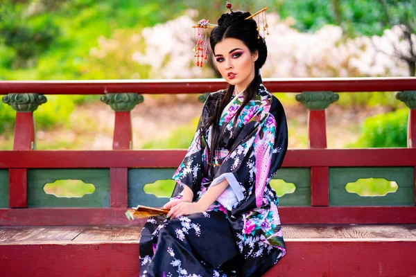 塔の近くの花の庭にポーズをとる髪と着物の棒を持つ美しいアジアのブルネットの女の子 日本の若いモデルの春の肖像画 — ストック写真