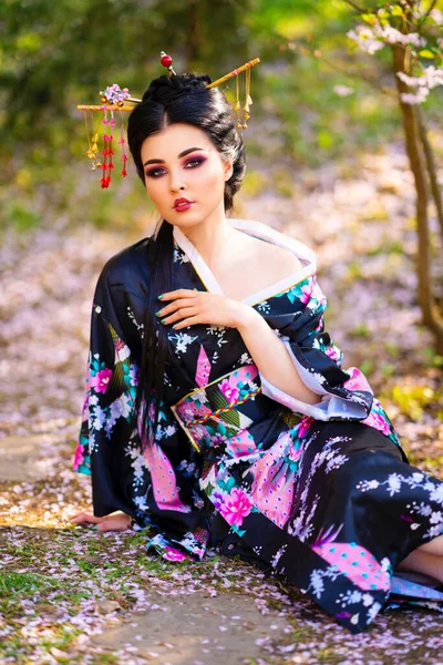 美しいアジアのブルネットの女の子は 髪と着物の棒で花の庭にポーズをとっています 日本の若いモデルの春の肖像画 — ストック写真