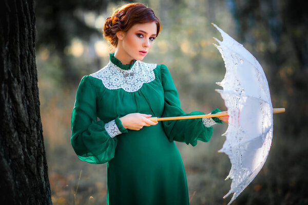 Beautiful red haired girl in green long vintage dress and basket of flowers standing with lace umbrella.Pretty tenderness model with perfect hairstyle dreaming and looking at camera.Art work and fairytale
