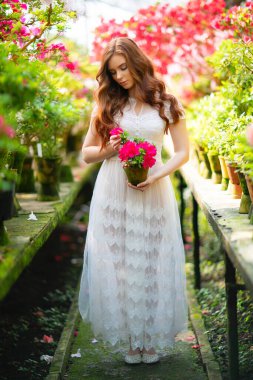 Renkli çiçeklerle dolu bir bahçede duran beyaz dantel elbiseli güzel kızıl saçlı kız. Romantik bir kadının sanat eseri. Sevecen bir model..