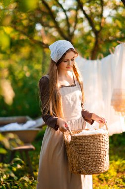 Ortaçağ kostümü giymiş güzel bir çamaşırcı köyde eski bir yalakla doğa elbiselerini yıkıyor. Kırsalda çalışan güzel bir kız. Peri masalı eserleri.