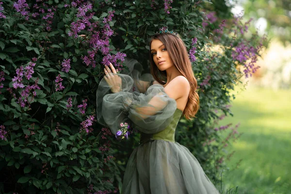 아름다운 왕관을 아름다운 녹색긴 드레스를 라일락 정원에 모델의 — 스톡 사진