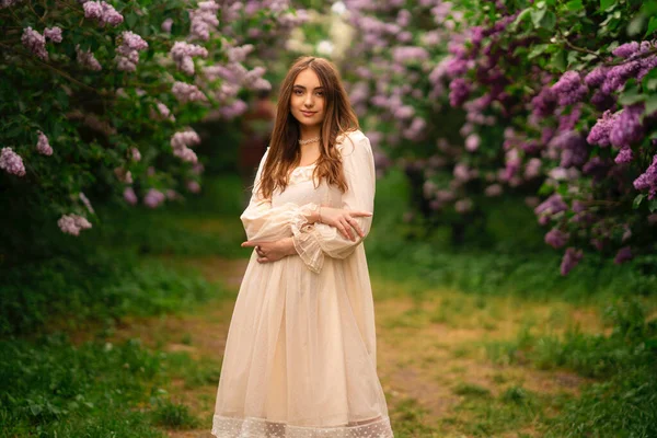 美丽的女孩 留着长发 穿着老式的白色衣服 在紫丁香花园里摆姿势 享受大自然的浪漫模式 — 图库照片