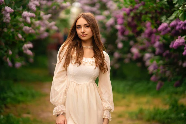 ライラックガーデンでポーズをとっている長い髪とヴィンテージの白いドレスを持つ美しい女の子 自然を楽しむロマンチックなモデル — ストック写真