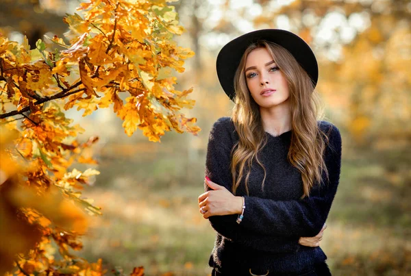 カラフルな秋の葉の近くに立って暗いドレスと黒の帽子の美しい女の子の肖像画を閉じます ロマンチックな女性のアート作品 カメラを見てかなり優しさモデル — ストック写真