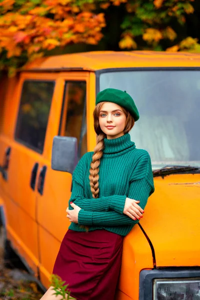 穿着绿色针织毛衣和贝雷帽的迷人模特站在秋天背景的老式复古橙色公共汽车旁边 五彩缤纷的艺术 — 图库照片