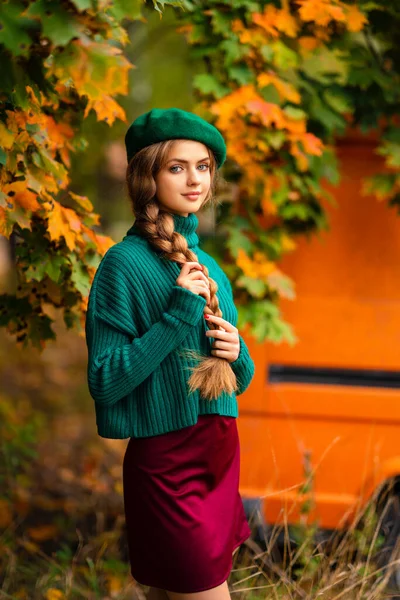 穿着绿色针织毛衣和贝雷帽的迷人模特站在秋天背景的老式复古橙色公共汽车旁边 五彩缤纷的艺术 — 图库照片