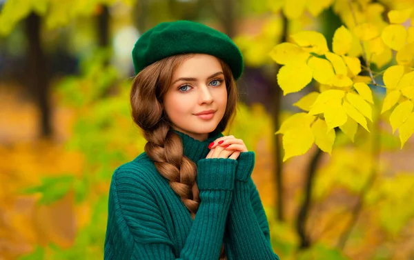 青い目と編組された髪を持つ若い美しいブロンドの少女の肖像画 緑の編まれたセーターと秋の自然に立っているベレーの魅力的なモデル カラーフルアート — ストック写真