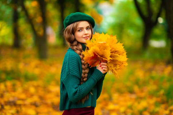 穿着绿色针织毛衣和贝雷帽的迷人模特 站在秋天的自然中 手里拿着叶束着花束 五彩缤纷的艺术 — 图库照片