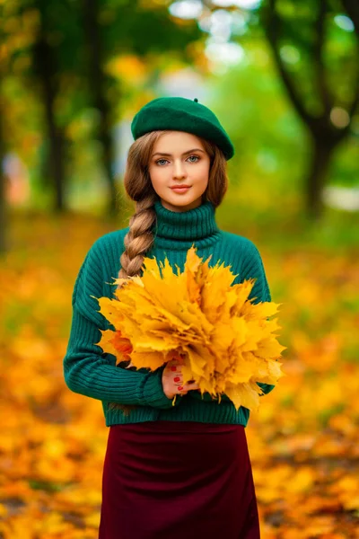 穿着绿色针织毛衣和贝雷帽的迷人模特 站在秋天的自然中 手里拿着叶束着花束 五彩缤纷的艺术 — 图库照片