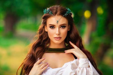 Ortaçağ elf elbisesi ve yeşil arka planda poz veren uzun pelerinli güzel kızıl saçlı prenses. Diadem 'deki savaşçı hakkında bir masal. Sıcak renkli sanat eserleri.