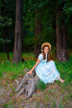 Hasır şapkalı, klasik elbiseli, yeşil arka planda poz veren güzel sarışın kıvırcık kız. Renkli, sıcak sanat eserleri üzerine şapkalı zarif bir bayan.. 