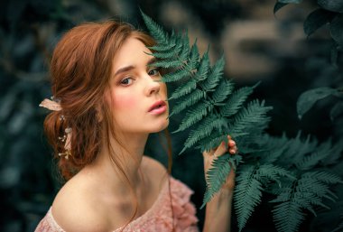 Renkli çiçeklerin yanında duran pembe, eski moda elbiseli güzel kızıl saçlı bir kızın portresini yakından çek. Romantik bir kadının sanat eseri. Kameraya bakan oldukça hassas bir model..