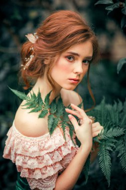 Renkli çiçeklerin yanında duran pembe, eski moda elbiseli güzel kızıl saçlı bir kızın portresini yakından çek. Romantik bir kadının sanat eseri. Kameraya bakan oldukça hassas bir model..