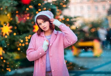 Örgü şapkalı güzel genç bir mankenin portresi Noel arkaplanının üzerinde bokeh ışıkları ile duruyor. Sihirli sıcak yeni yıl fotoğrafı. Kış fuarının samimi arka planı. Mutlu kadın..