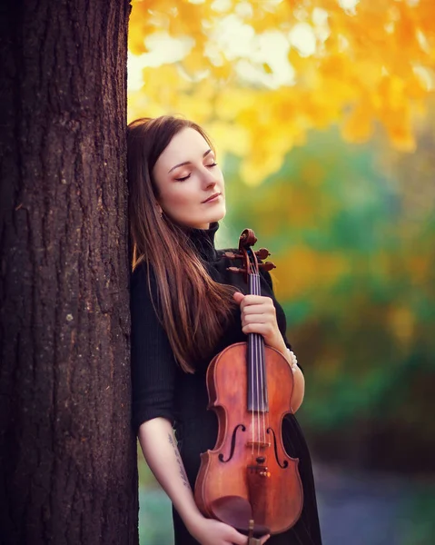 ヴァイオリンのダークドレスで美しいブルネットの女の子の肖像画 秋の公園に黄色い背景に悲しい目を持つヴァイオリニスト — ストック写真