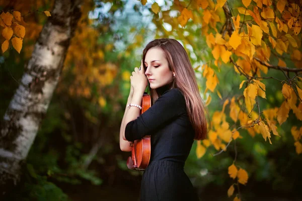 一个穿着深色衣服 带着小提琴的漂亮的黑发女孩的画像 秋天公园里紧闭双眼的拥抱小提琴 — 图库照片