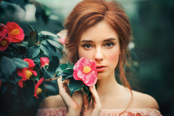Close up portrait of a beautiful red hair girl in a pink vintage dress standing near colorful flowers. Art work of romantic woman .Pretty tenderness model looking at camera.