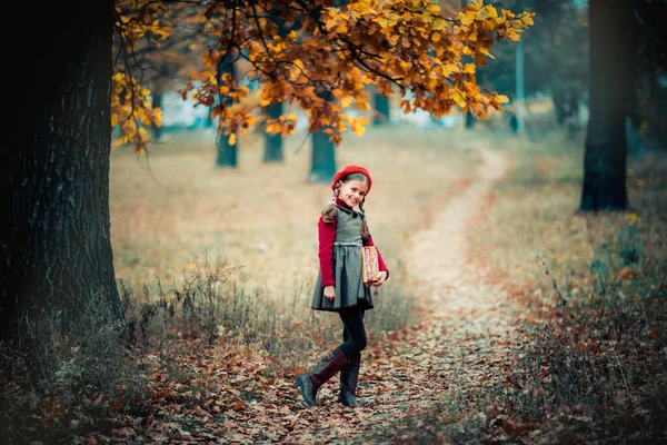 一个身穿红色贝雷帽 头戴辫子 头戴书本的漂亮女学生的秋天画像 温柔积极的孩子 带着灿烂的笑容在公园里享受大自然 — 图库照片
