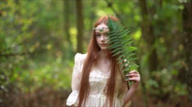 Ortaçağ elbisesiyle parlayan güneşte taç takan güzel kızıl saçlı kız. Prenseslerle ilgili bir masal. Ormanda eğreltiotu tutan bir model. Sıcak sanat eserleri.