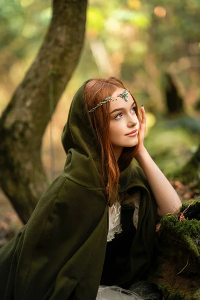 一个美丽的红头发女孩穿着绿色中世纪衣服在苔藓树附近的画像 精灵的童话故事 森林中惊人的造型 温暖的艺术作品 — 图库照片
