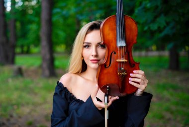 Yeşil parkta elinde keman tutan siyah elbiseli güzel sarışın kız. Sanat eserleri. Üzgün kadın rüya görüyor..