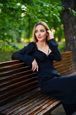 Yeşil parkta oturan siyah elbiseli güzel sarışın kız. Sanat eserleri. Üzgün kadın rüya görüyor..