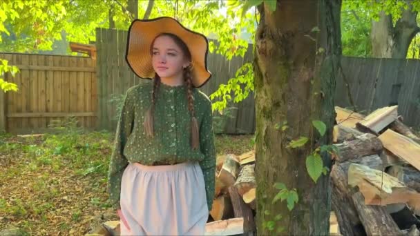 美丽的女孩 留着辫子 穿着老式衣服 头戴一顶帽子 站在木柴旁 阳光明媚的大自然上 一个农场少女 蓝眼睛童话般的故事 — 图库视频影像