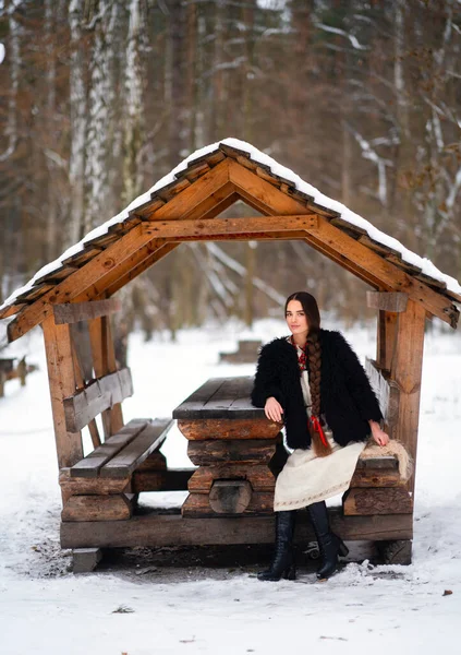 ウクライナの伝統的なドレス 黒い毛皮のコートおよび冬の森でポーズする赤いビーズの美しい余分長編組の髪の少女 冬の背景に若い魅力的なスタイリッシュな女性の肖像画 — ストック写真
