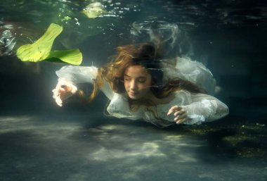 Güzel sarışın, uzun saçlı, beyaz elbiseli yeşil bitkilerle gölde poz veren kız. Ophelia hakkındaki peri masalı. Sıcak sanat eserleri.