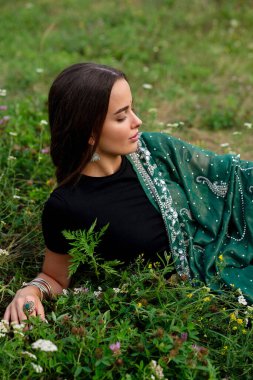 Nehir kenarında poz veren, ekstra uzun örgülü, Hint geleneksel elbiseli güzel esmer kız. Yeşil doğa arka planında, sari içinde genç ve çekici bir kadının portresi..