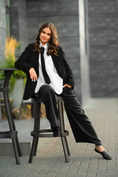 stock image Beautiful teenager girl posing on streets wearing jacket and tie dress. Young model on photo in business style.