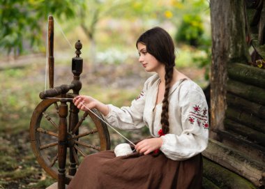 Kırsal, uzun Ukrayna elbisesi içinde örülmüş güzel esmer kız çarkla doğa üzerinde çalışıyor. Kırsal kesimdeki sanat fotoğraflarında oldukça genç bir model.. 