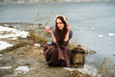 Ortaçağ elbisesi içinde güzel kızıl saçlı bir kızın portresi ve nehrin yanındaki karlı ormanda yünlü bir eşarp. Kırsal kesimde, elinde tahta kovayla genç bir işçi. Renkli masal sanatı.