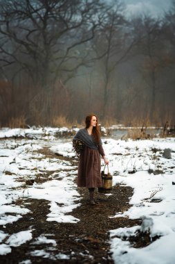 Ortaçağ elbisesi içinde güzel kızıl saçlı bir kızın portresi ve nehrin yanındaki karlı ormanda yünlü bir eşarp. Kırsal kesimde, elinde tahta kovayla genç bir işçi. Renkli masal sanatı.