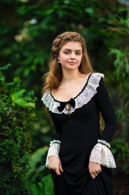 Siyah elbiseli, dantel elbiseli, yeşil bahçeli güzel bir kız. Romantik bir kadının sanat eseri. Doğanın tadını çıkaran şefkatli bir model..