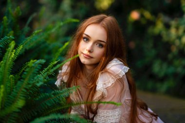 Yeşil bitkiler ve eğrelti otunun yanında duran pembe klasik elbiseli ve hasır şapkalı güzel bir kız. Romantik bir kadının sanat eseri. Bahçede poz veren sevimli bir model..