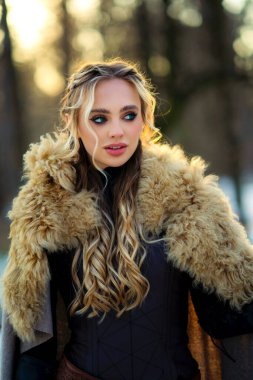 Ortaçağ kürklü elbiseli güzel sarışın kız kış güneşli ormanlarda poz veriyor. Savaşçı hakkında bir masal. Sıcak sanat eserleri.