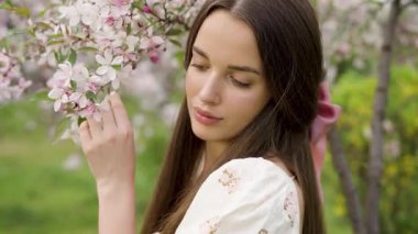 Ekstra uzun siyah saçlı genç bir kadının çiçek açan kiraz ve sakura bahçesinde yürüdüğü güzel bir sanat videosu. Klasik elbise, romantik bahar atmosferi, yumuşak doğal ışık, huzurlu ve rüya gibi bir sahne..