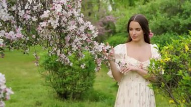 Ekstra uzun siyah saçlı genç bir kadının çiçek açan kiraz ve sakura bahçesinde yürüdüğü güzel bir sanat videosu. Klasik elbise, romantik bahar atmosferi, yumuşak doğal ışık, huzurlu ve rüya gibi bir sahne..