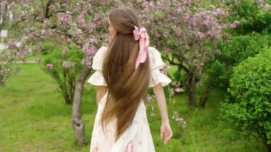 Ekstra uzun siyah saçlı genç bir kadının çiçek açan kiraz ve sakura bahçesinde yürüdüğü güzel bir sanat videosu. Klasik elbise, romantik bahar atmosferi, yumuşak doğal ışık, huzurlu ve rüya gibi bir sahne..