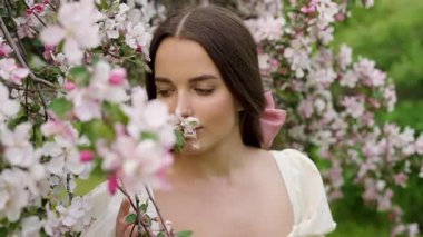 Ekstra uzun siyah saçlı genç bir kadının çiçek açan kiraz ve sakura bahçesinde yürüdüğü güzel bir sanat videosu. Klasik elbise, romantik bahar atmosferi, yumuşak doğal ışık, huzurlu ve rüya gibi bir sahne..