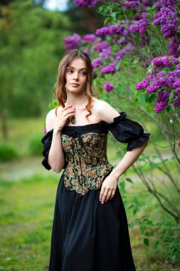 Çiçekli leylak bahçesinde poz veren klasik korse giymiş romantik bir kadın.