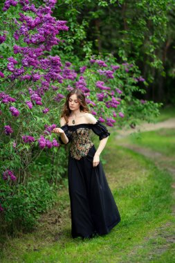 Çiçekli leylak bahçesinde poz veren klasik korse giymiş romantik bir kadın.