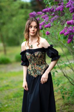 Çiçekli leylak bahçesinde poz veren klasik korse giymiş romantik bir kadın.
