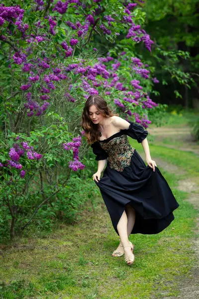 Çiçekli leylak bahçesinde poz veren klasik korse giymiş romantik bir kadın.