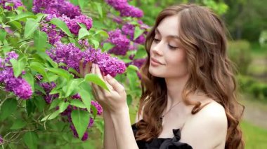 Çiçekli leylak bahçesinde poz veren klasik korse giymiş romantik bir kadının videosu.