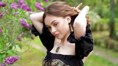Çiçekli leylak bahçesinde poz veren klasik korse giymiş romantik bir kadının videosu.